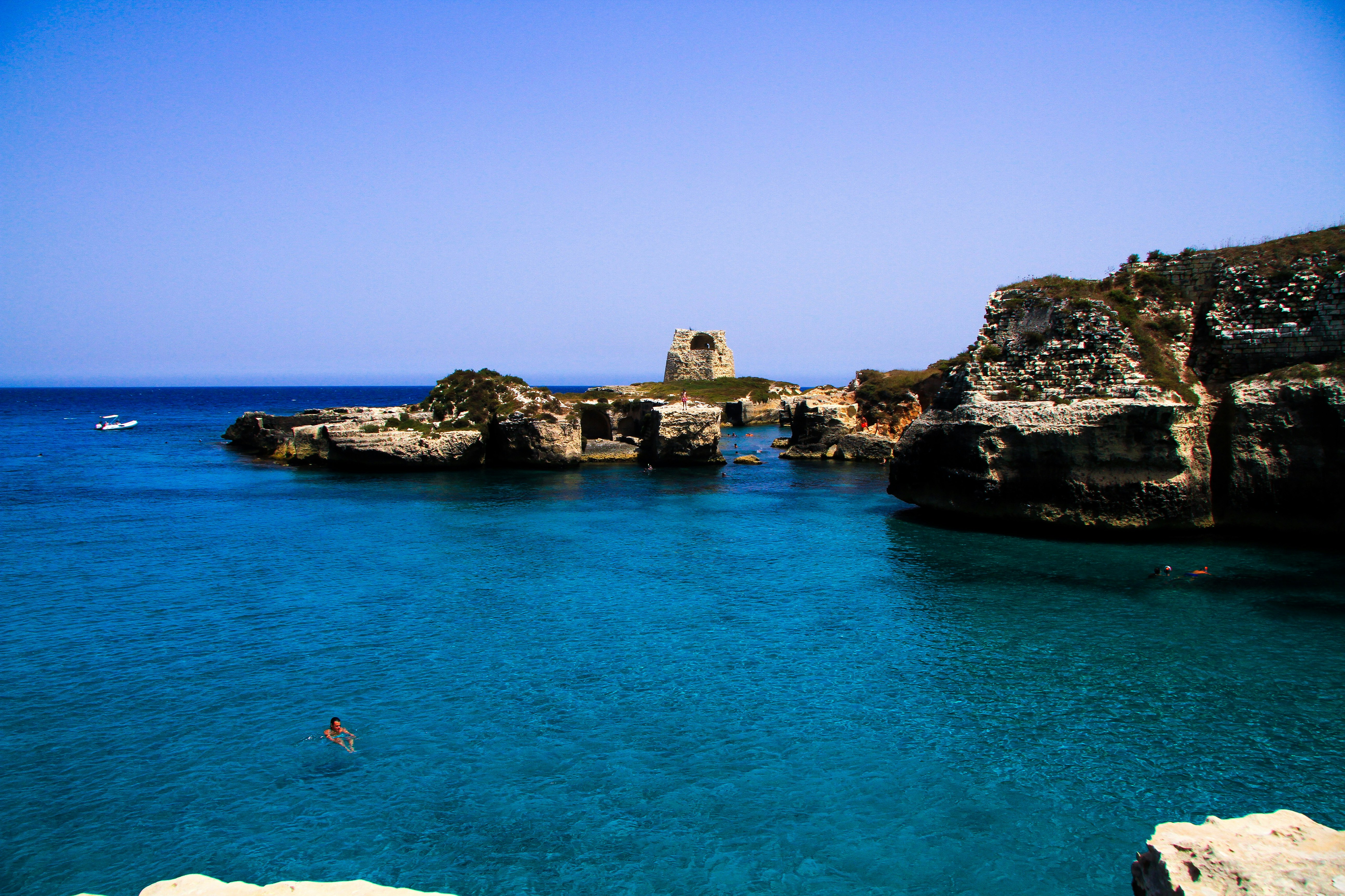 person in white shirt on blue sea near brown rock formation during daytime